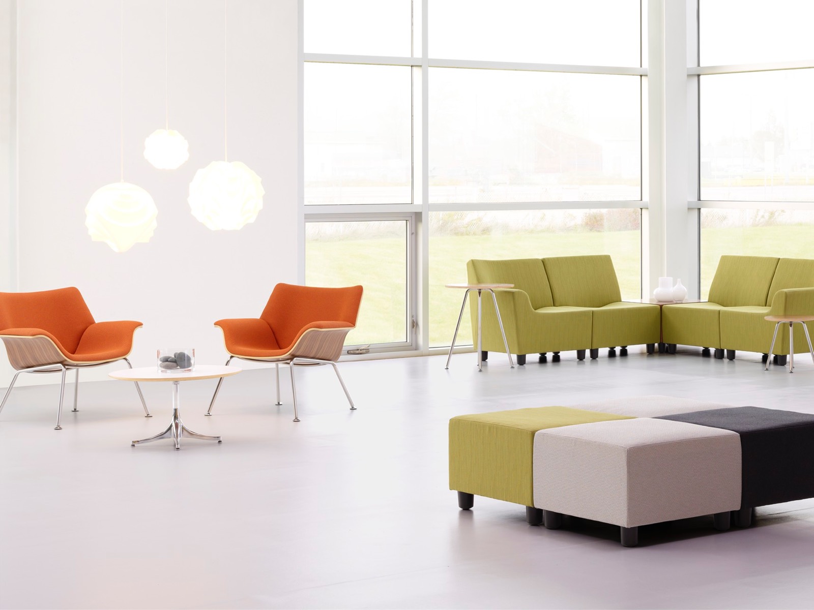 Oranje Swoop loungestoelen en groene Swoop modulaire zitplaatsen in een informele verzamelruimte.